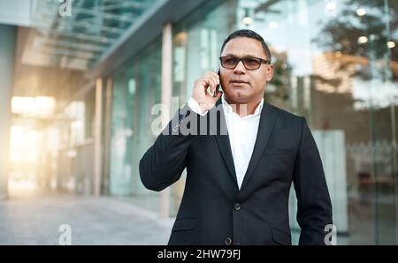 Dammi la notizia Scatto corto di un bel uomo d'affari maturo che fa una telefonata con il suo ufficio in background. Foto Stock