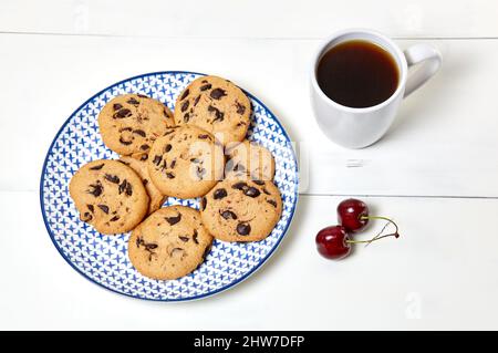 Tazza bianca con caffè, biscotti tradizionali e ciliegie dolci su sfondo bianco di legno, primo piano. Colazione gustosa, concetto di routine mattutino Foto Stock