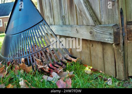 Mucchio di foglie e un rastrello appoggiato contro una recinzione autunno sfondo Foto Stock