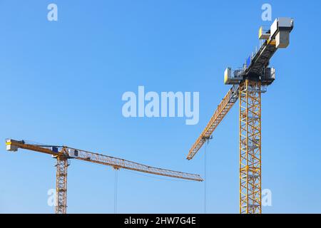 Due gru gialle su un cantiere contro il cielo blu, spazio copia, fuoco selezionato, profondità di campo stretta Foto Stock