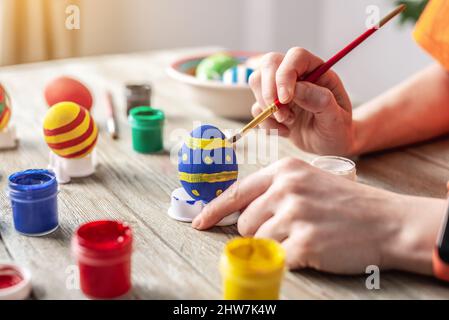 La mano della donna con un pennello sta disegnando un motivo colorato su un uovo di Pasqua. Preparazione per la luminosa vacanza di Pasqua. Foto Stock