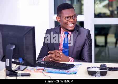 uomo d'affari adulto seduto al computer portatile in ufficio con le dita incrociate e guardando da parte sorridente. Foto Stock