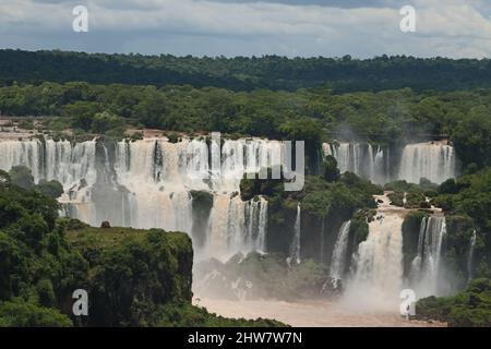 Vista ravvicinata della piattaforma di osservazione e dei ponti per i turisti delle cascate Cataratas sotto il cielo blu, l'arcobaleno e una nebbia d'acqua al Foz do Iguassu pa Foto Stock