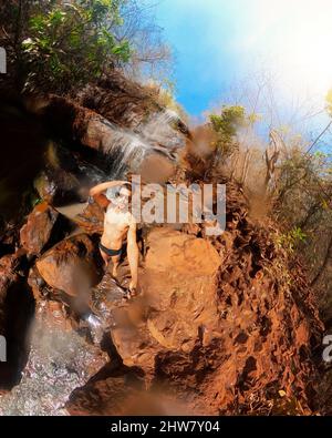 Uomo in occhiali e bunks nuoto alla cascata con 360 fotocamera in una giornata di sole Foto Stock