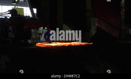 Primo piano del processo di forgiatura del metallo presso la fabbrica. Il martello idraulico forma la billetta calda rossa, la produzione di parti metalliche. Foto Stock