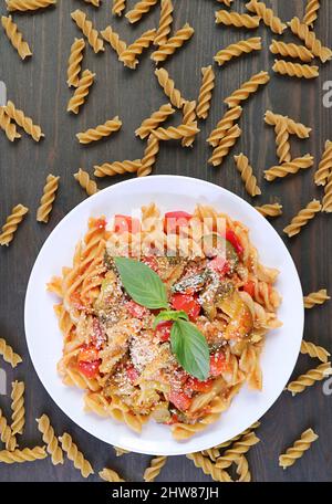 Piatto di succulenta pasta di Fusilli di frumento intero in salsa di pomodoro con pasta secca sparsa intorno Foto Stock