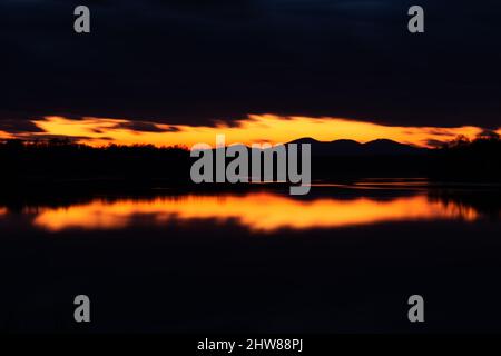 Ultima luce nel cielo sopra la silhouette di montagna incorniciata da nuvole scure al crepuscolo - paesaggio con riflessione simmetrica sulla superficie dell'acqua Foto Stock