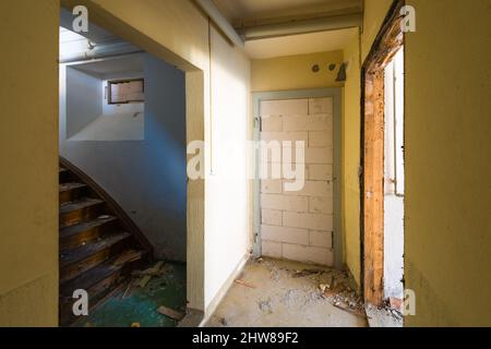 Corridoio in una casa in rovina. Scale fino all'uscita. Porta murata mattone. Il concetto - uscire da una situazione difficile. Foto Stock