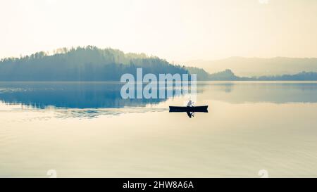 Nebbia sul lago. In acqua calma specchio di riflessione. Uomo con una pagaia in barca. Bianco e nero. Foto Stock