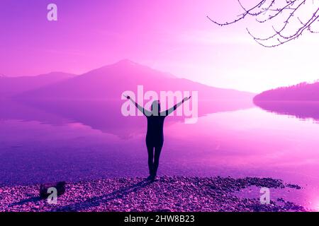 Figura femminile con bracci aperti larghi. Fantastiche vette naturali di montagna riflesse nelle acque del lago. La luce del sole. Foto Stock