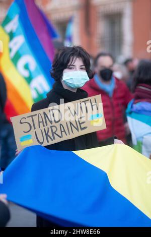 Massa, Italia - 26 febbraio 2022 - Girl ondeggia la bandiera Ucraina tenendo un cartello con l'iscrizione Stand with Ukraine Foto Stock