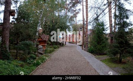 Bellissimo piccolo villaggio con cottage in mattoni situato in luogo ecologico. Video. Seguendo il sentiero di ghiaia lungo alberi in crescita e case in estate d Foto Stock