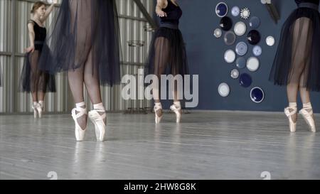 Primo piano di ballerine danzanti in abiti neri e scarpe bianche a punta. Azione. Le ballerine si preparano per balletto e ballano splendidamente in balli neri Foto Stock
