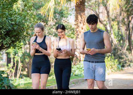 Tre giovani atleti stanno camminando concentrati sul loro telefono nel parco Foto Stock