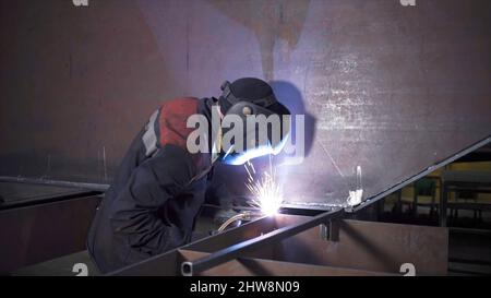 Il saldatore lavora in fabbrica su una struttura metallica. Clip. Lavori di saldatura con metallo in fabbrica. Impianti metallurgici e lavori di saldatura. Foto Stock