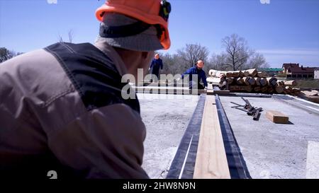 Lavoratori di tavole di legno di misura in cantiere. Clip. I costruttori fanno le misure dei pannelli per la costruzione della casa di legno. Foto Stock