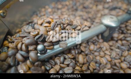 Primo piano dei chicchi di caffè mescolati e tostati. Azione. La macchina speciale mescola i chicchi di caffè per la lavorazione termica. Tostatura del caffè in macchina. Foto Stock