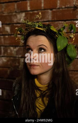 Giovane donna che indossa una corona in foglia verde naturale sullo sfondo della parete di mattoni Foto Stock