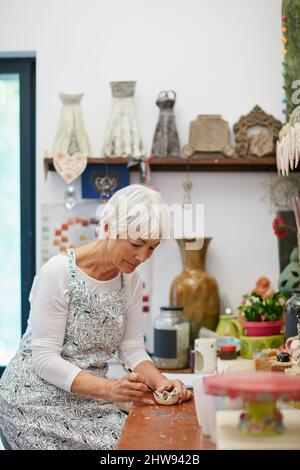 Il suo angolo di astuto. Shot di una donna anziana che fa una pentola di ceramica in un laboratorio. Foto Stock