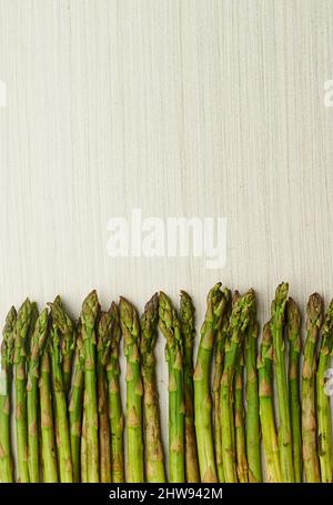 Tenero e pronto a mangiare. Taglio corto di lance di asparagi verdi adagiate su una superficie di legno chiaro. Foto Stock