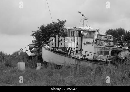 Foto in bianco nero di una vecchia barca bagnata a riva con il mare e il cielo nuvoloso sullo sfondo Foto Stock