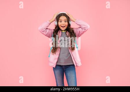 ragazza teen stupita con zaino che indossa le cuffie su sfondo rosa, musica Foto Stock