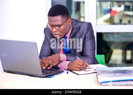 bel uomo d'affari in giacca seduta alla scrivania che lavora con un computer portatile e un notebook. Foto Stock