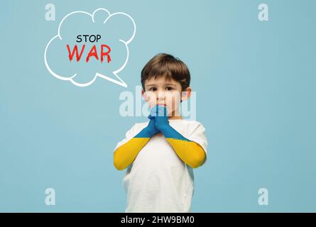 Immagine concettuale con ragazzino, bambino con le mani ricoperte di colori della bandiera ucraino isolato su sfondo blu con scritte Foto Stock