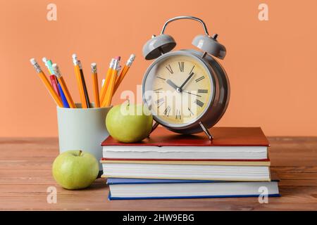 Pila di libri, sveglia, matite e mele su tavola di legno Foto Stock