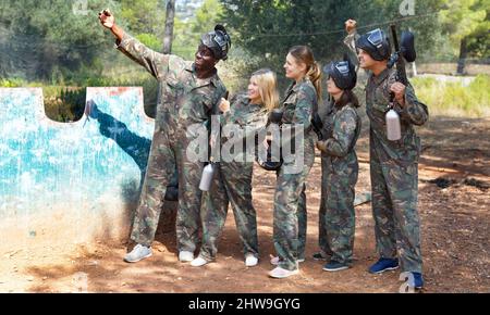 Allegro gruppo di giocatori di paintball con attrezzatura completa che fanno selfie con smartphone all'aperto Foto Stock