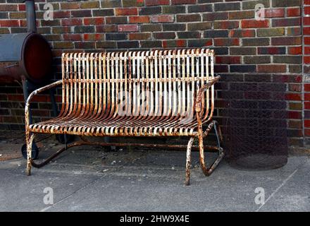 L'aliante rustico, con superficie arrugginita e verniciata, funge da posto a sedere in questo vicolo posteriore. La griglia e il cestello in filo metallico si trovano su ciascun lato di Foto Stock