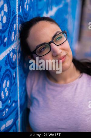 Giovane e bella donna si appoggia contro un muro colorato e si pone per la macchina fotografica - stile di strada tipico Foto Stock