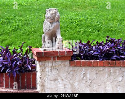 Il maestoso leone di cemento si erge su una recinzione di mattoni e Malta a Memphis, Tennessee. Le piante viola crescono intorno alla recinzione. Foto Stock