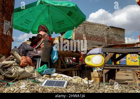 Un venditore di strada siede vicino al suo commercio di strada mentre carica la sua lampada ad energia solare nelle baraccopoli di Kibera. Nelle baraccopoli di Kibera, la maggior parte dei residenti, in particolare i venditori ambulanti, le scuole private, le organizzazioni non governative, le luci di strada e le scuole, utilizzano tutti il sistema di energia solare a basso costo, che è una fonte di energia più affidabile e a basso costo. Ciò ha reso più facile il riciclaggio della maggior parte dell'energia elettrica consumata dai residenti e ha anche contribuito a ridurre l'elevato numero di morti che si verificano a causa delle scosse elettriche e degli incendi di slum quotidiani. Foto Stock