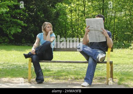 coppia litigante seduta a parte su una panca del parco, legge il giornale, lo guarda espettantly Foto Stock