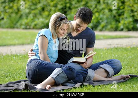 la giovane coppia si siede a piedi nudi in un prato e leggendo un libro insieme Foto Stock