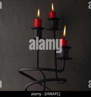 Candele rosse che bruciano in candelabri contro una parete scura Foto Stock