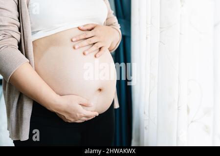 Primo piano della donna incinta con il ventre grande alla finestra. Gravidanza, maternità, persone e concetto di aspettativa. Madre. Foto Stock