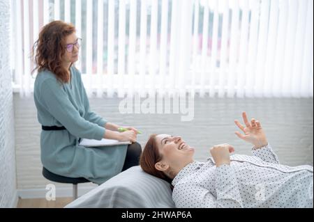 Una donna di mezza età si trova su un divano e parla con uno psicologo. Foto Stock