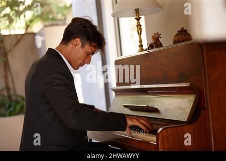 Perdendosi nella musica. Scatto di un bel giovane che suona il pianoforte a casa. Foto Stock
