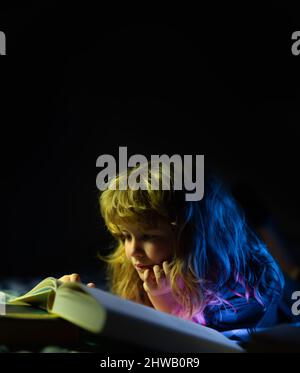 Bambino che legge un libro magico a letto. Bambino ragazzo leggere libri a casa. Concetto di educazione e lettura. Foto Stock