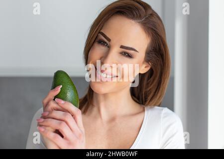 Allegro giovane 30s caicasiano donna che tiene avocado in casa Foto Stock
