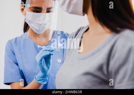 Donna asiatica medico che tiene la siringa e che usa il cotone prima di fare l'iniezione alla gente del paziente in maschera medica. Vaccino Covid-19 o coronavirus Foto Stock