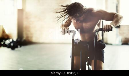 Dandogli tutto ciò che ha ottenuto. Scatto ritagliato di un bel giovane uomo che guarda pieno di determinazione mentre si allenano su un addestratore ellittico. Foto Stock