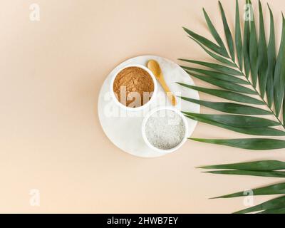 Cosmetici rossi e blu polvere di argilla in ciotole su vassoio di marmo e foglia di palma verde su sfondo beige. Vista dall'alto. Spazio di copia Foto Stock