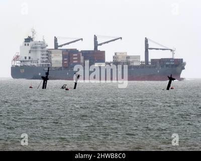 Sheerness, Kent, Regno Unito. 5th Mar 2022. Storico naufragio della SS Richard Montgomery raffigurato da 3 angolazioni sulla marea ultrabassa di questa mattina (altezza prevista 0,31m) che affondò 1,5 miglia a Sheerness nel Kent nel 1944. I tre montanti e i due rack di poppa possono essere visti su queste maree ultra basse (normalmente si vede solo il rack di poppa in avanti). I 3 alberi saranno tagliati quest'estate. PIC: Guardando Nord-Est dal lungomare vicino ai moli di Sheerness. Container nave 'Mariner' nel canale del Tamigi che passa che ha anche 3 montanti di movimentazione del carico. Credit: James Bell/Alamy Live News Foto Stock