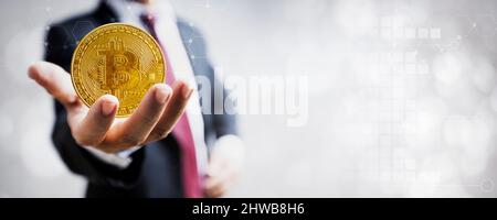 Bitcoin criptovaluta, moneta d'oro a mano d'uomo d'affari e uno sfondo grafico sfocato Foto Stock