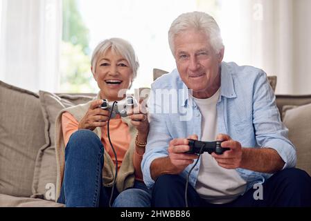 Hanno così tanto divertimento giocare i video giochi. Scatto di una coppia anziana che gioca video giochi. Foto Stock