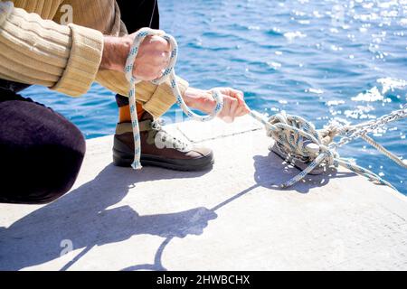 mani forti di un marinaio accovacciato che legano le corde della nave e nodi di legatura sul molo di ormeggio di un porto Foto Stock