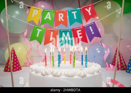 Candele bruciate su torta su palloncini e nastri sfondo. Torta bianca con candele per la festa di compleanno. Foto Stock